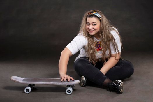 Beautiful plump woman with a skateboard on a gray background.