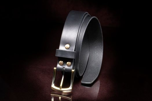 Leather belt with a metal buckle close-up on a dark background.