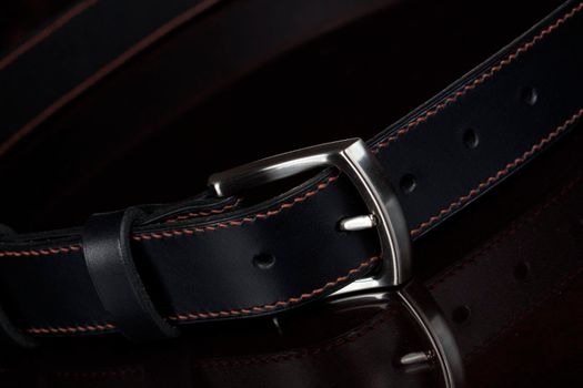 Leather belt with a metal buckle close-up on a dark background.