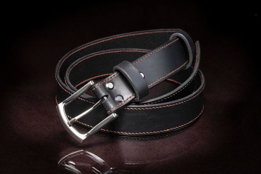 Black leather belt with a metal buckle on a dark background close-up.