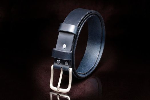 Leather belt with a metal buckle close-up on a dark background.