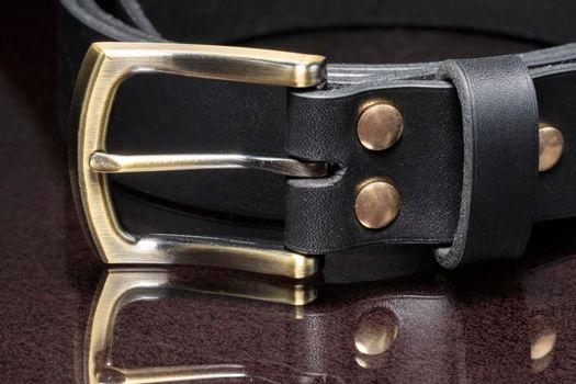 Leather belt with a golden buckle on a dark background close-up.