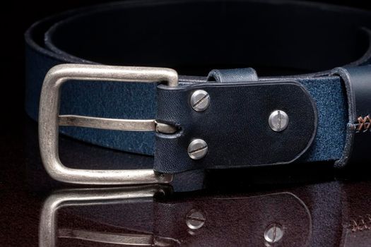Leather belt with a metal buckle close-up on a dark background.