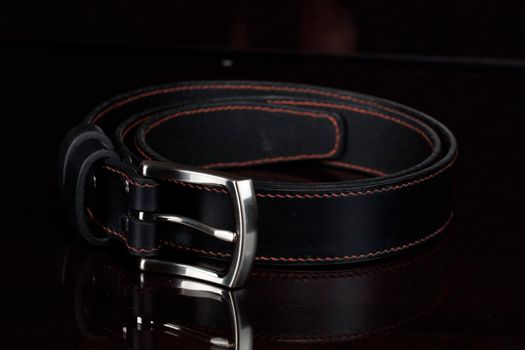 Black leather belt with a metal buckle on a dark background close-up.