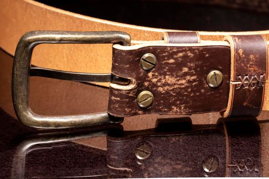 Brown leather belt with scuffs and a metal buckle on a dark background.