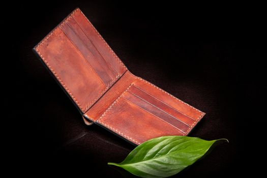 Leather brown open purse and green leaf on a dark background.