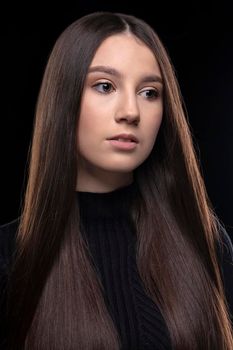 A beautiful young girl with long straight hair on a dark background does not look into the camera.