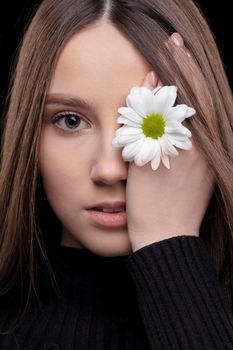 A beautiful girl with natural beauty holds a white flower near her eye. Young girl with a white chrysanthemum.