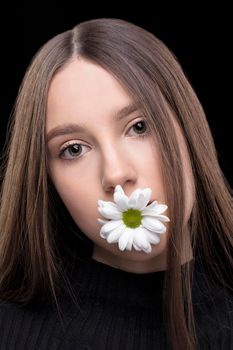 A beautiful girl with natural beauty holds a white flower in her mouth. Young girl with a white chrysanthemum.