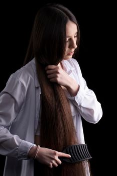 A beautiful brunette girl combs her long smooth hair on a dark background.