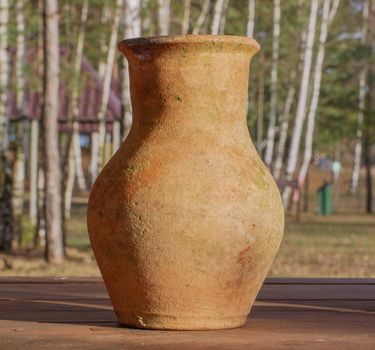 Light brown earthenware homemade jug on a blurred background of trees.