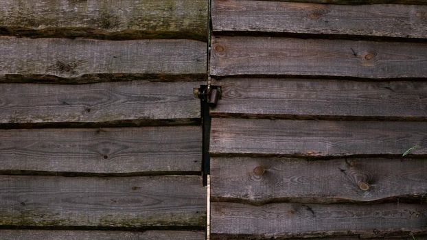 A wooden fence and a gate made of planks with a lock. Wooden board fence with doors.