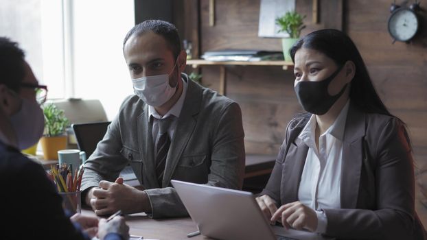 Multi-Ethnic Team Of Business People In Medical Masks Meetings In Modern Office During Quarantine, Coworkers Talks Keeping A Social Distance Due To Coronavirus Outbreak, Pandemic Concept