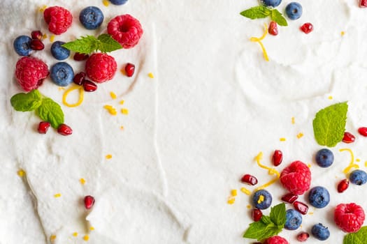 Whipped cream from egg whites with raspberries, blueberries, pomegranate. Composition of berries with place for text on a white background. Layout. View from above.