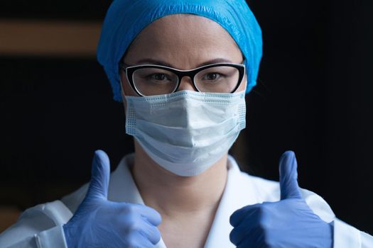 Female Doctor Medical Worker In White Protective Uniform And Surgical Mask Gestures Thumbs Up Showing That Everything Will Be Fine, Medical Laboratory Employee Reports About Good Test Results
