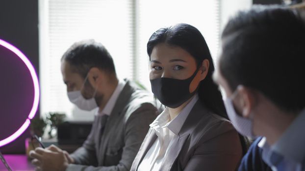 Diverse Team Of Business People Communicate Wearing Face Protection Working In Modern Office During Quarantine, Selective Focus On Asian Woman Looking On Her Male Companion, Epidemic Concept