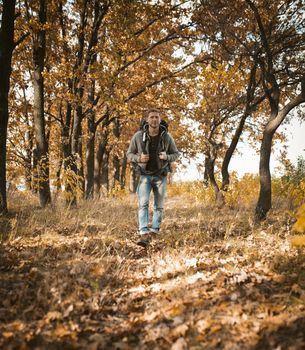 Young Traveler Walking Along In Autumn Forest, Happy Caucasian Man With Big Backpack Walks Along A Forest Path On Outskirts Of Field, He Admires The Beauty Of Nature Traveling Outdoors On Sunny Day