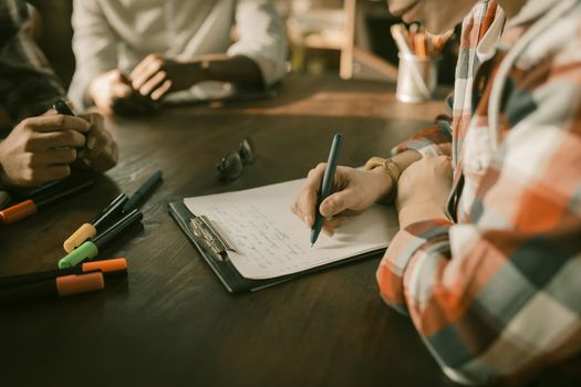 Brainstorming Team Of Freelancers, Close Up Shot Of Woman's Hands Writing Ideas With A Pen On A Paper Stationery Sitting At Wooden Table With Multi-Colored Markers On It, Start Up Concept