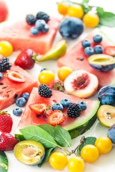 variation of summer berries and fruits cutted in pieces on white wooden background