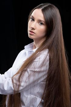 Beautiful young girl with long straight hair in a white shirt posing in the studio on a gray background