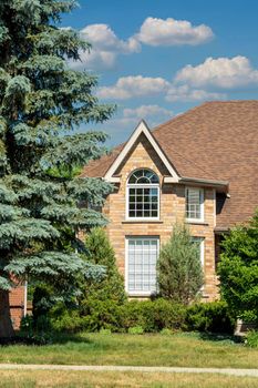 Fragment of a house with an attic and blue spruce under white clouds