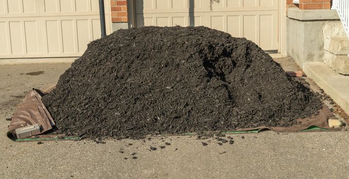 A pile of black mulch for plants and paths near the flower bed, poured onto the asphalt near the garage