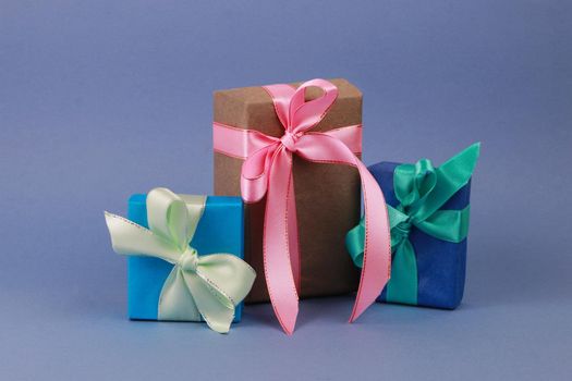 Two blue and one brown gift boxes with bows on a blue paper background. A holiday concept. A gift for Valentine's Day. A gift for Mother's Day. Birthday gift.