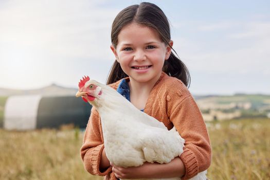 an adorable little girl holding a chicken on a farm.