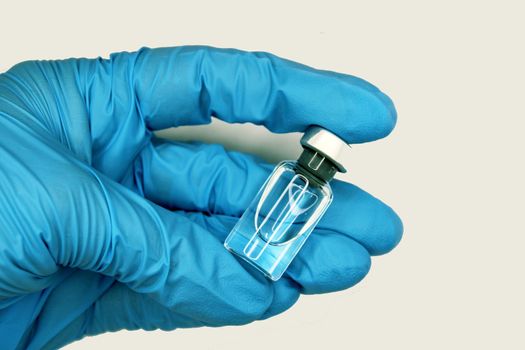 A hand in a blue medical glove close-up holding a vaccine against a light background. The concept of the fight against Covid19..