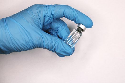 A hand in a blue medical glove close-up holding a vaccine against a light background. The concept of the fight against Covid19..