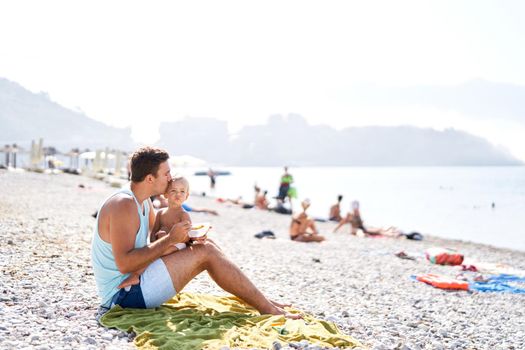 Dad kisses his little daughter while feeding on the beach. High quality photo