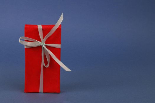 Beautiful red gift box with white ribbon on blue paper background. Holiday concept. Christmas gift. Valentine's day gift. Birthday gift.