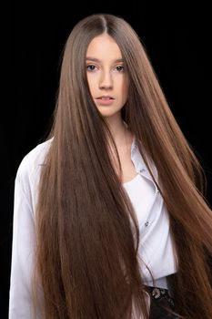 Vertical portrait of a beautiful girl with very long luxurious hair on a dark background.