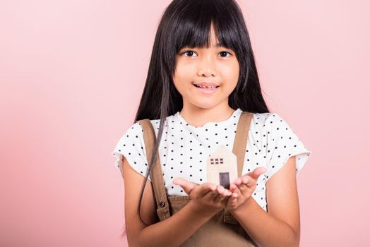 Asian little kid 10 years old hold wood house model on hands at studio shot isolated on pink background, Happy child girl with home model