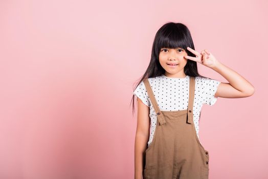 Asian little kid 10 years old show v-sign fingers gesture at studio shot isolated on pink background, Happy child girl lifestyle making victory symbol sign