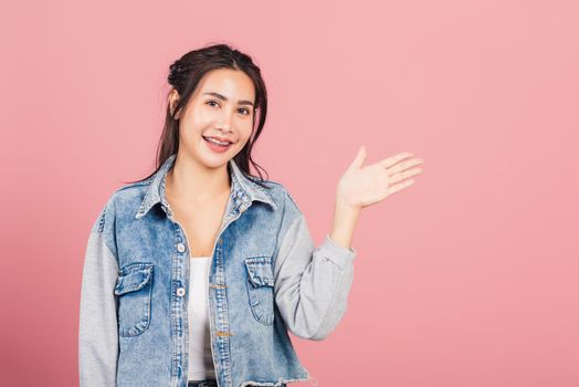 Asian happy portrait beautiful cute young woman smile standing presenting product holding something on palm away side, studio shot isolated on pink background with copy space, female show hand gesture