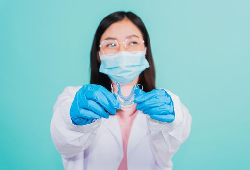 Asian beautiful woman dentist holding silicone orthodontic retainers for teeth on hand isolated blue background, Teeth retaining tools after removable braces, Orthodontics dental healthy care concept