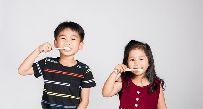 Little cute kid boy and girl 3-6 years old brushing teeth and smile in studio shot isolated on white background, happy Asian children holding toothbrush in mouth by himself, Dental hygiene healthy