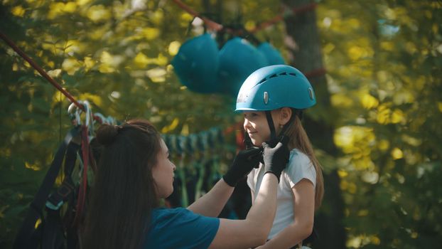 Woman instructor helping a little girl putting on helmet. Mid shot