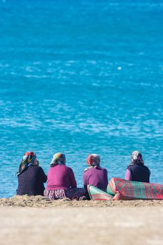 Four turkish vilage women in national authentic costume and headscarf sits on the carpet at the coast of sea beach, and talking