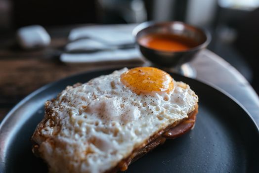 Toast with cheese and sausage covered with fried egg on a plate. Selective focus. Top view.