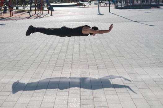 A man in black sportswear jumps doing push-ups in the park