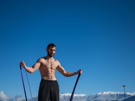 Shirtless man doing exercise with rubber bands outdoors