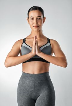 Studio portrait of a sporty young woman meditating against a grey background.