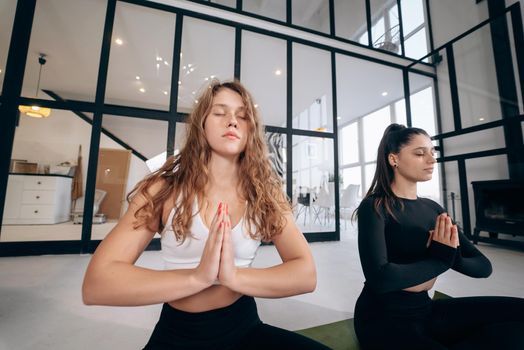 Two young women meditating in lotus pose with hands in namaste. Yoga