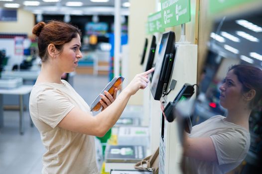 A frustrated woman uses a self-checkout counter. The girl does not understand how to independently buy groceries in the supermarket without a seller.