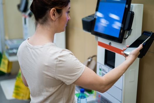 Woman paying with smartphone in store at self-checkout counter