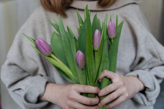 Close-up of a young woman wearing a beige jumper and holding a bunch of pink tulips