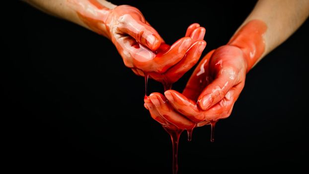 Women's hands in a viscous red liquid similar to blood