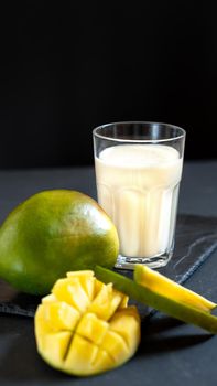 Milk drink on black background with mango. A classic mango milkshake - Lassi. A traditional drink in India from the heat.